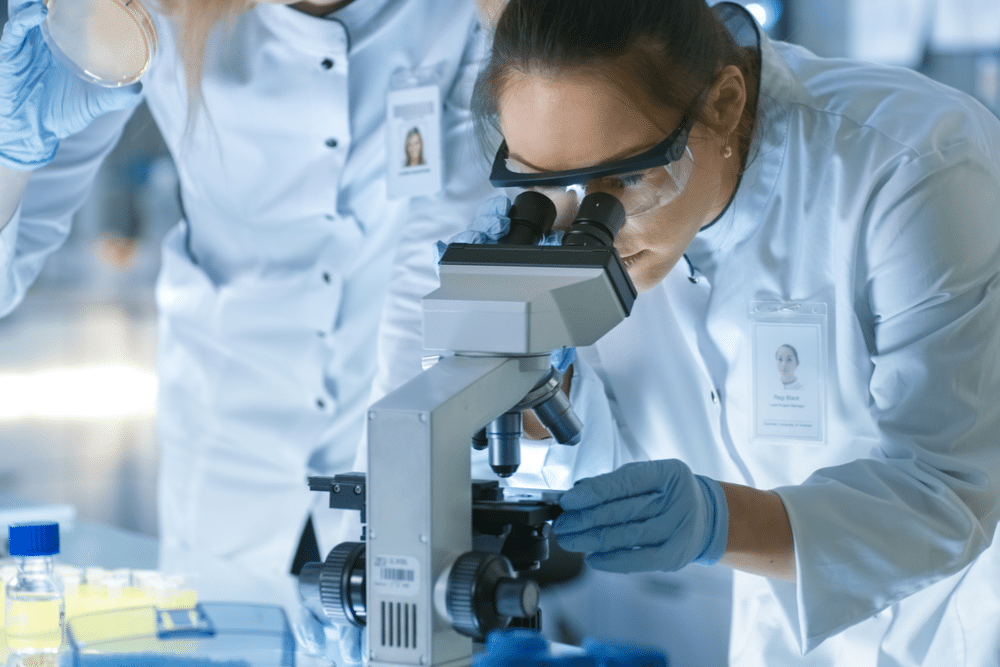 Medical Research Scientist Drops Sample on Slide and Her Colleague Examines it Under Microscope.