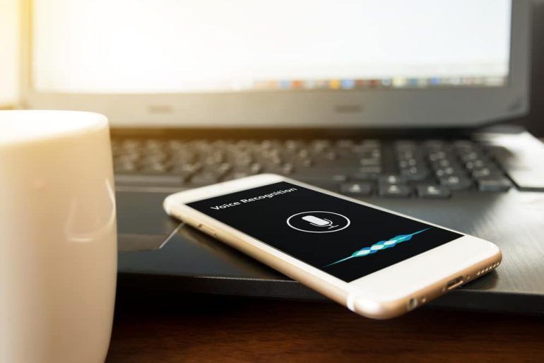 A laptop, smart speaker and a phone laying on a desk