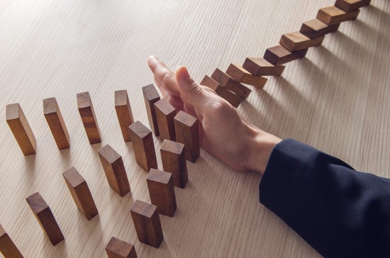 A hand stopping domino blocks from falling