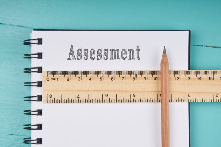 ssessment word on notebook, wooden ruler and pencil on blue wooden background. Top view. Business concept.