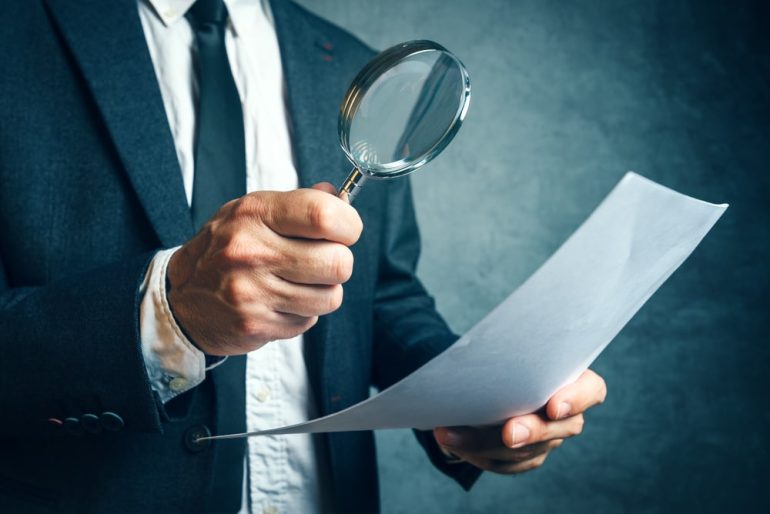 Tax inspector investigating offshore company documents and papers with magnifying glass, forensic accounting concept