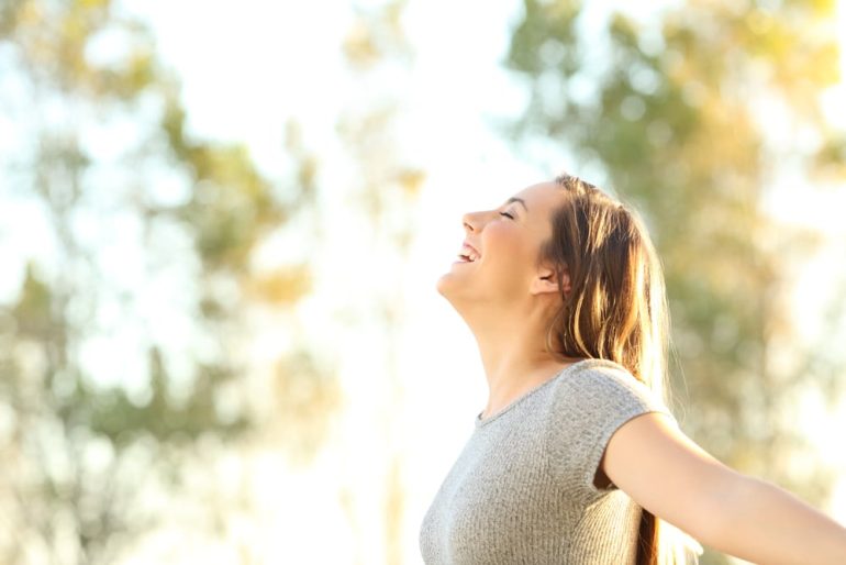 Side view portrait of a woman breathing fresh air outdoors in summer with trees and sky in the background