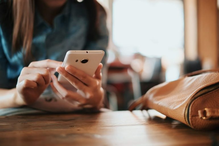 Hand of woman using smartphone on wooden table,Space for text or design.