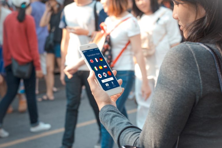 obile translation application concept.Young tourist using mobile phone on blurred people walking at street as background
